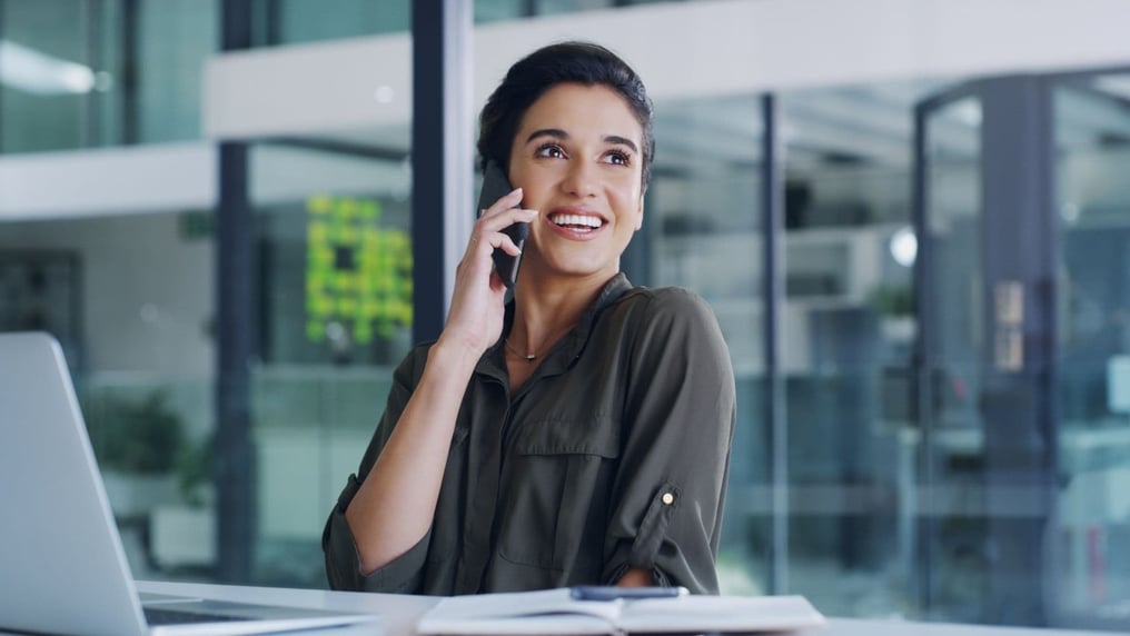 Eine lächelnde brünette Frau spricht am Telefon mit einem Kunden, symbolisiert die Bedeutung von Sprachkommunikation im Geschäftsalltag.