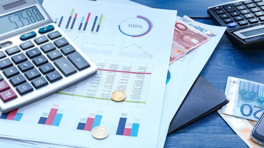 Office desk with charts printed on A4 paper, mobile phone, calculator, banknotes and coins.